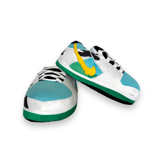 Low Moo Moo Sneaker Slippers – plush cow-print sneaker-style slippers for kids with teal soles and yellow swoosh accents on white background.